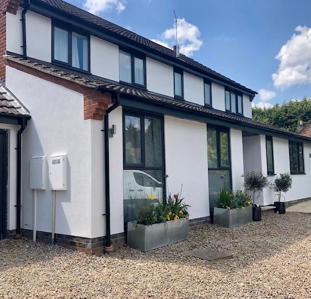 Two-storey house finished in white render with dark window frames