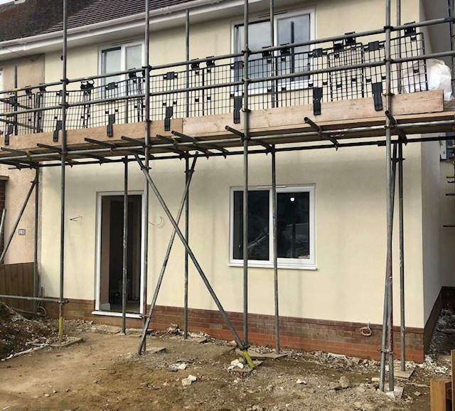 Two-storey wall freshly rendered in cream with the scaffolding still in place