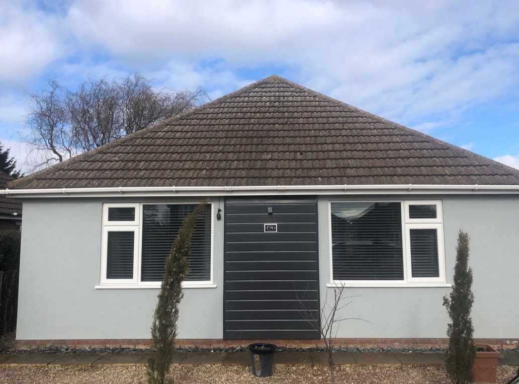 Bungalow in light grey render with a dark cladding panel by the door